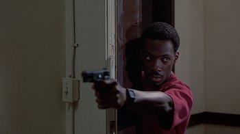 Movie still from “Beverly Hills Cop” (1984), directed by Martin Brest – A man holding a gun in front of a door; Close Up shot, Low angle