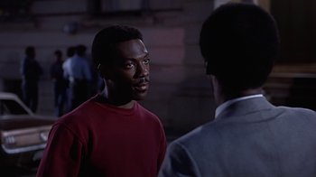 Movie still from “Beverly Hills Cop” (1984), directed by Martin Brest – A man in a red shirt talking to another man in a gray suit; Close Up shot, Over the shoulder angle
