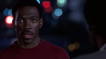 Movie still from “Beverly Hills Cop” (1984), directed by Martin Brest – A man in a red shirt is standing in the dark; Close Up shot, Over the shoulder angle