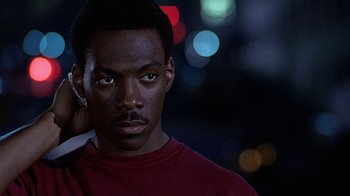 Movie still from “Beverly Hills Cop” (1984), directed by Martin Brest – A young man is standing in front of some lights; Close Up shot, Over the shoulder angle