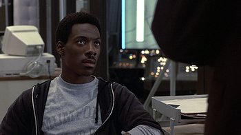 Movie still from “Beverly Hills Cop” (1984), directed by Martin Brest – A man sitting at a table in front of a window; Close Up shot, Over the shoulder angle
