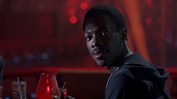 Movie still from “Beverly Hills Cop” (1984), directed by Martin Brest – A man sitting at a table with a drink in front of him; Close Up shot, Over the shoulder angle