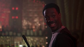 Movie still from “Beverly Hills Cop” (1984), directed by Martin Brest – A man smiles while holding a microphone; Close Up shot, Low angle