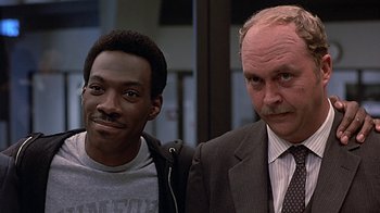 Movie still from “Beverly Hills Cop” (1984), directed by Martin Brest – A man in a suit standing next to another man in a suit; Close Up shot, Over the shoulder angle