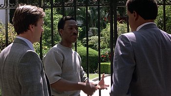 Movie still from “Beverly Hills Cop” (1984), directed by Martin Brest – A group of men standing next to each other near a fence; Medium shot, Over the shoulder angle