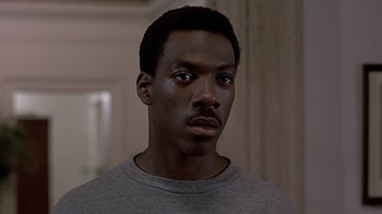 Movie still from “Beverly Hills Cop” (1984), directed by Martin Brest – A person wearing a gray t - shirt; Close Up shot, Over the shoulder angle