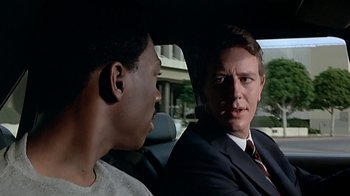 Movie still from “Beverly Hills Cop” (1984), directed by Martin Brest – A man in a suit talking to another man in a car; Close Up shot, Over the shoulder angle