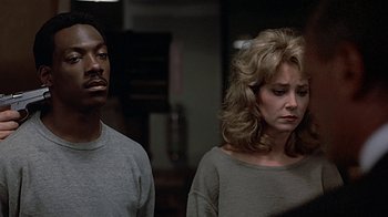 Movie still from “Beverly Hills Cop” (1984), directed by Martin Brest – A man and a woman standing next to each other in a room; Close Up shot, Over the shoulder angle