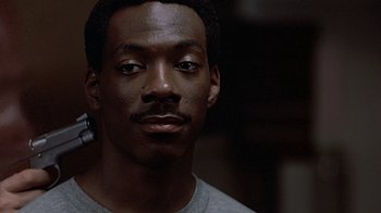 Movie still from “Beverly Hills Cop” (1984), directed by Martin Brest – A person wearing a gray t - shirt; Close Up shot, Over the shoulder angle