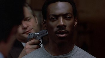 Movie still from “Beverly Hills Cop” (1984), directed by Martin Brest – A man holding a gun up to his face; Close Up shot, Over the shoulder angle