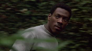 Movie still from “Beverly Hills Cop” (1984), directed by Martin Brest – A man in a gray shirt is in the woods; Close Up shot, High angle