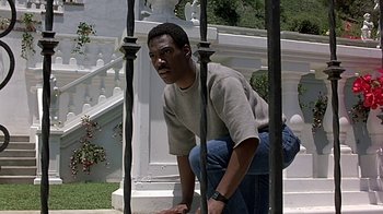 Movie still from “Beverly Hills Cop” (1984), directed by Martin Brest – A man kneeling on the ground in front of a building; Medium shot, Low angle