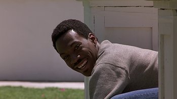 Movie still from “Beverly Hills Cop” (1984), directed by Martin Brest – A man smiling for the camera while leaning against a wall; Close Up shot, High angle