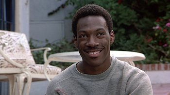 Movie still from “Beverly Hills Cop” (1984), directed by Martin Brest – A person sitting in front of a table; Close Up shot, Over the shoulder angle
