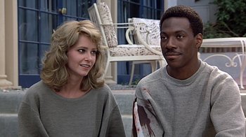 Movie still from “Beverly Hills Cop” (1984), directed by Martin Brest – A man and a woman standing next to each other; Medium shot, Over the shoulder angle