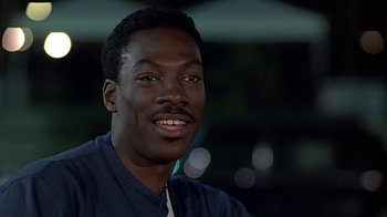 Movie still from “Beverly Hills Cop” (1984), directed by Martin Brest – A person smiling for the camera; Close Up shot, Over the shoulder angle