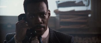 Movie still from “Beverly Hills Cop II” (1987), directed by Tony Scott – A man in a suit and tie holding a microphone; Close Up shot, Low angle