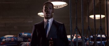 Movie still from “Beverly Hills Cop II” (1987), directed by Tony Scott – A man in a suit and tie standing in front of lights; Medium shot, Low angle