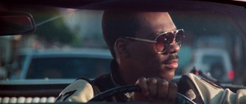 Movie still from “Beverly Hills Cop II” (1987), directed by Tony Scott – A man in a car holding a steering wheel; Close Up shot, Low angle
