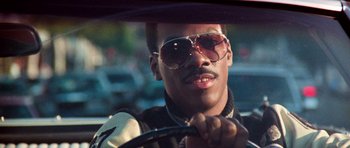 Movie still from “Beverly Hills Cop II” (1987), directed by Tony Scott – A man driving a car wearing sunglasses and holding a steering wheel; Close Up shot, Low angle