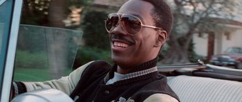 Movie still from “Beverly Hills Cop II” (1987), directed by Tony Scott – A person wearing sunglasses and a vest; Close Up shot, Over the shoulder angle