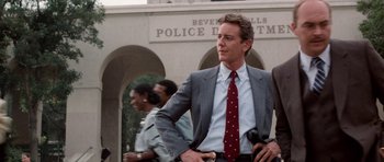 Movie still from “Beverly Hills Cop II” (1987), directed by Tony Scott – A man in a gray suit and a red tie; Medium shot, Low angle