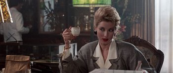 Movie still from “Beverly Hills Cop II” (1987), directed by Tony Scott – A woman holding a coffee cup while sitting at a table; Medium shot, Over the shoulder angle