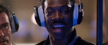 Movie still from “Beverly Hills Cop II” (1987), directed by Tony Scott – A person wearing headphones and smiling; Close Up shot, Over the shoulder angle