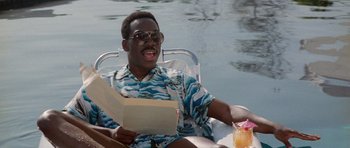 Movie still from “Beverly Hills Cop II” (1987), directed by Tony Scott – A man sitting in a chair with a drink and holding a letter; Medium shot, High angle