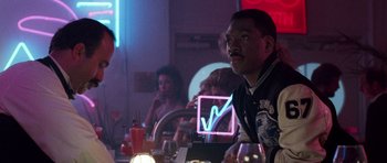 Movie still from “Beverly Hills Cop II” (1987), directed by Tony Scott – A man sitting at a table in front of other people; Medium shot, Over the shoulder angle