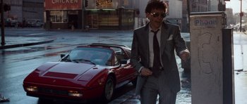 Movie still from “Beverly Hills Cop II” (1987), directed by Tony Scott – A man in a suit and tie standing next to a red car; Medium shot, Low angle