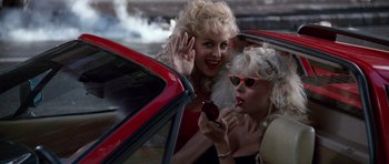 Movie still from “Beverly Hills Cop II” (1987), directed by Tony Scott – Two women in a red car waving to the camera; Medium shot, Over the shoulder angle
