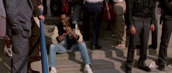 Movie still from “Beverly Hills Cop II” (1987), directed by Tony Scott – A man sitting on some steps with a camera in his hand; Medium shot, High angle