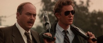 Movie still from “Beverly Hills Cop II” (1987), directed by Tony Scott – A man holding a gun next to another man in a suit; Close Up shot, Low angle