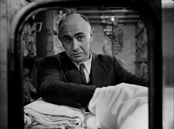 Movie still from “Bicycle Thieves” (1948), directed by Vittorio De Sica – A man in a suit and tie sitting in front of a mirror; Medium shot, Low angle