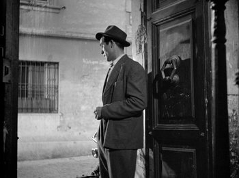 Movie still from “Bicycle Thieves” (1948), directed by Vittorio De Sica – A black and white photo of a man standing in front of a door; Medium shot, Low angle