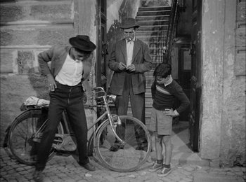 Movie still from “Bicycle Thieves” (1948), directed by Vittorio De Sica – A group of people standing around a bicycle; Wide shot, Over the shoulder angle