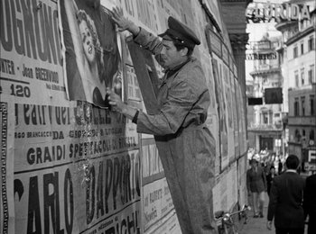 Movie still from “Bicycle Thieves” (1948), directed by Vittorio De Sica – An old photo of a man putting up a poster on the side of a building; Medium shot, Low angle