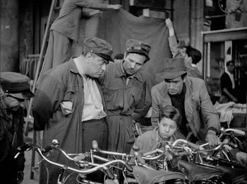 Movie still from “Bicycle Thieves” (1948), directed by Vittorio De Sica – A black and white photo of a group of men looking at bikes; Wide shot, High angle