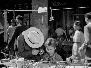 Movie still from “Bicycle Thieves” (1948), directed by Vittorio De Sica – An old black and white photo of a man and a boy at an outdoor market; Medium shot, Over the shoulder angle