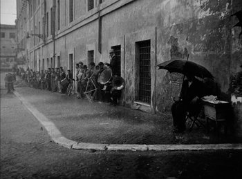 Movie still from “Bicycle Thieves” (1948), directed by Vittorio De Sica – A black and white photo of people waiting in line; Wide shot, High angle