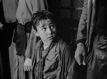 Movie still from “Bicycle Thieves” (1948), directed by Vittorio De Sica – A young boy is standing in front of two older men; Medium shot, Over the shoulder angle