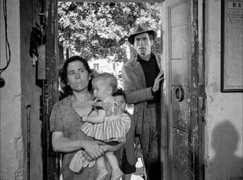 Movie still from “Bicycle Thieves” (1948), directed by Vittorio De Sica – An old black and white photo of a woman holding a baby; Wide shot, Over the shoulder angle