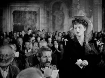 Movie still from “Bicycle Thieves” (1948), directed by Vittorio De Sica – An old photo of a woman standing in front of an audience; Medium shot, Over the shoulder angle