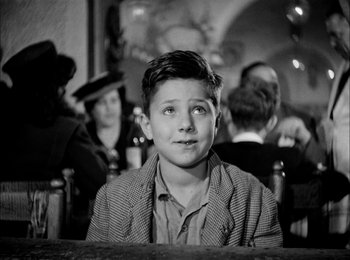 Movie still from “Bicycle Thieves” (1948), directed by Vittorio De Sica – A young boy sitting in front of a group of people; Medium shot, Low angle