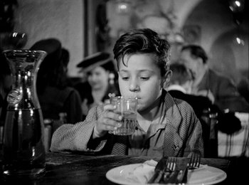 Movie still from “Bicycle Thieves” (1948), directed by Vittorio De Sica – A young boy drinking a glass of water at a restaurant; Medium shot, Over the shoulder angle