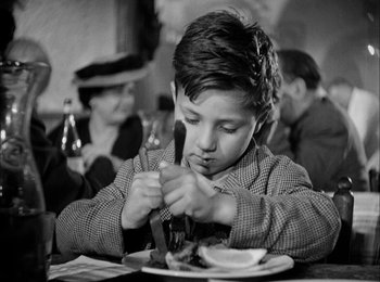 Movie still from “Bicycle Thieves” (1948), directed by Vittorio De Sica – A young boy sitting at a table eating a meal; Medium shot, Low angle