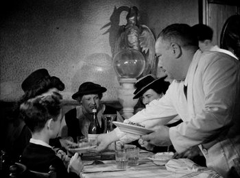 Movie still from “Bicycle Thieves” (1948), directed by Vittorio De Sica – A black and white photo of a group of people sitting at a table; Medium shot, Over the shoulder angle