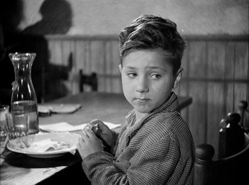 Movie still from “Bicycle Thieves” (1948), directed by Vittorio De Sica – A young boy sitting at a table in front of a plate of food; Medium shot, Over the shoulder angle