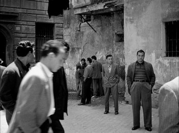 Movie still from “Bicycle Thieves” (1948), directed by Vittorio De Sica – A black and white photo of a group of men standing on a street; Wide shot, Low angle